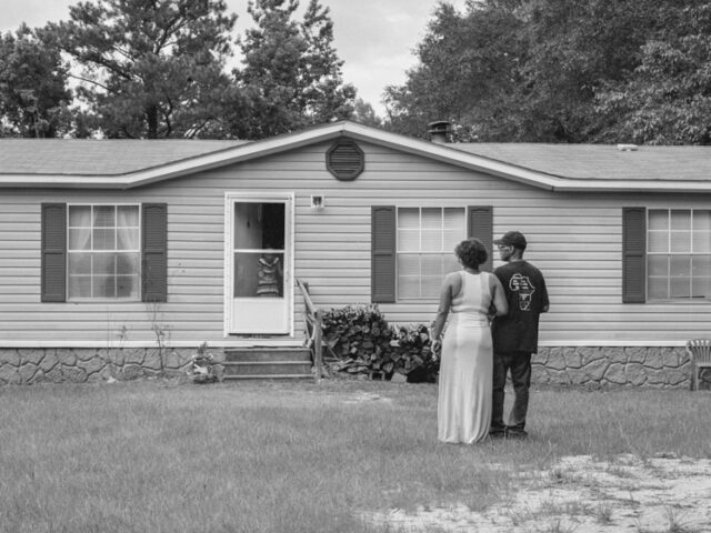 Black and white photo of two people with their back to the camera looking at a modular home.